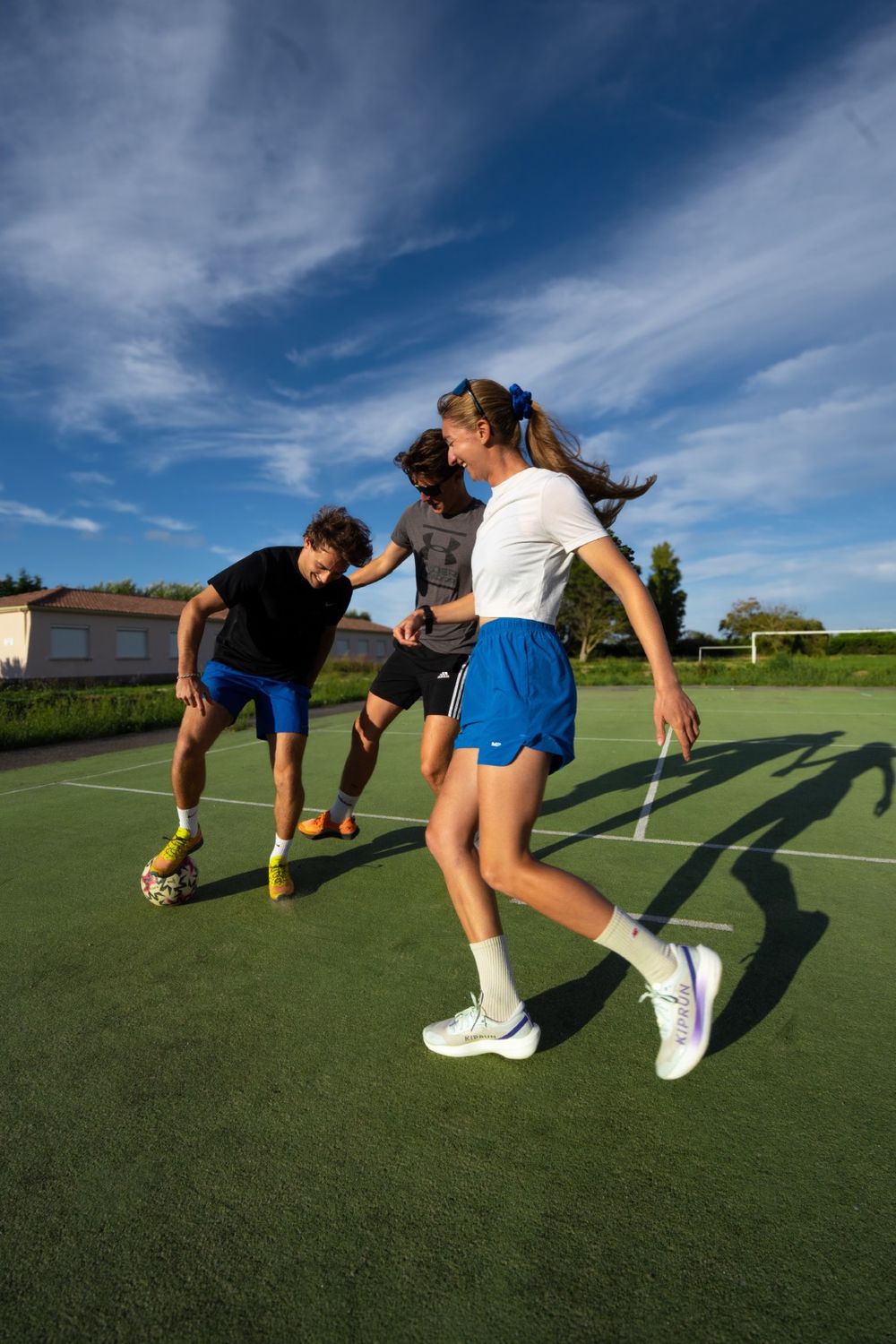 Trois amis jouent au foot sur un terrain synthétique